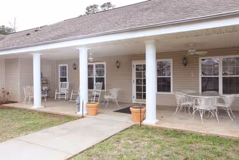 Covered porch with white columns, outdoor seating, and glass doors along a single-story building.
