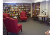 A cozy library-style common room with bookshelves along the walls, red wingback chairs, a globe, and small tables with lamps.