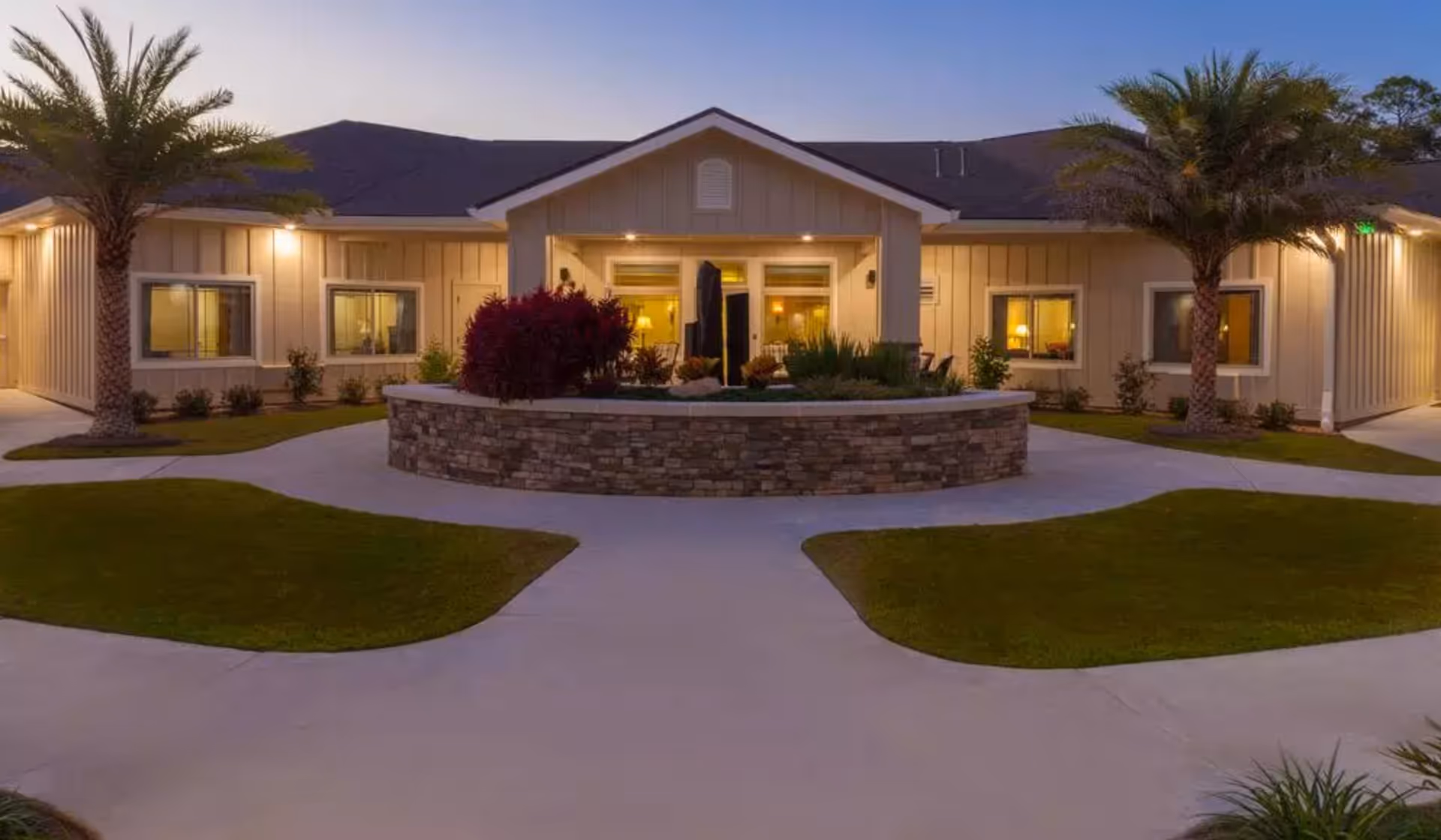 Exterior view of a memory care facility with a circular stone planter and palm trees.