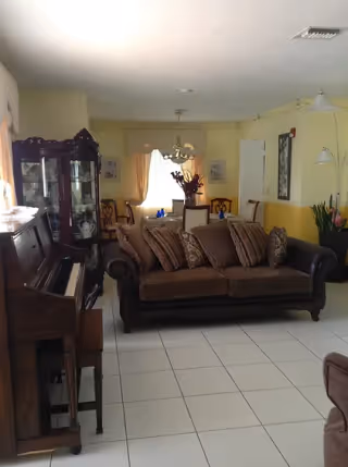 Cozy living room with a sofa, piano, china cabinet and dining table visible in the background.