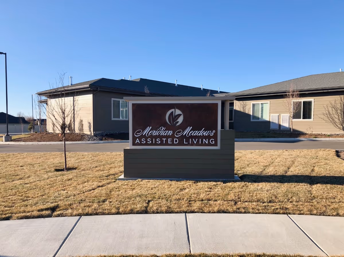 Outdoor view of Meridian Meadows Assisted Living facility sign on a grassy area with buildings in the background under a clear blue sky.