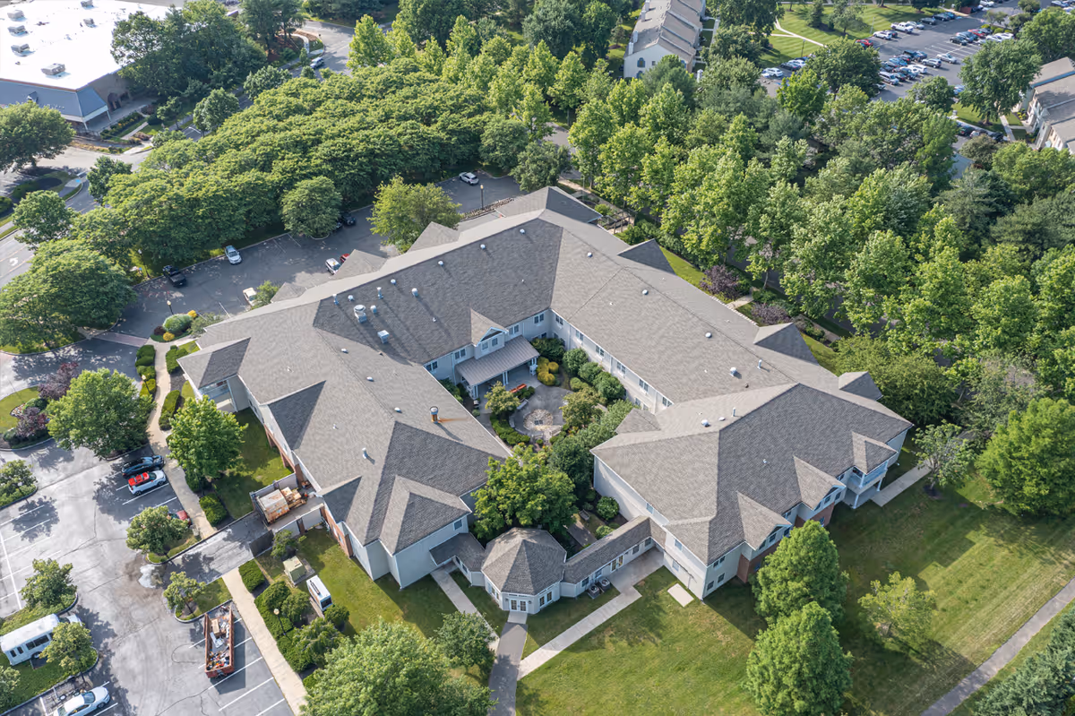 Aerial view of a large senior living facility named Rose Hill surrounded by trees and greenery, with a central courtyard garden and adjacent parking lots.
