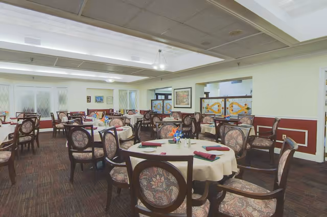 Formal dining room with round tables set with tablecloths and upholstered chairs.
