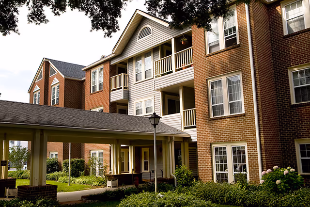 An exterior view of First Colonial Inn, showcasing multiple stories with brick and wooden siding and a landscaped entrance.