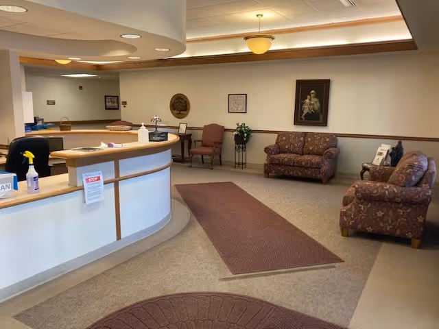 Reception lobby with a curved front desk, cushioned sofas and chairs, carpeting, and wall artwork.