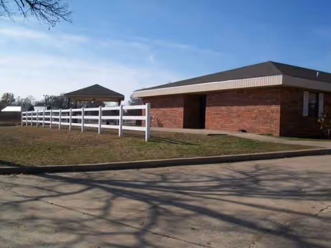 Exterior view of Southern Pointe Living Center: brick building, white fence, and gazebo on lawn.