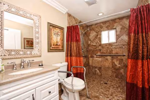 A bathroom in a senior living facility with sink, toilet, and tiled shower.