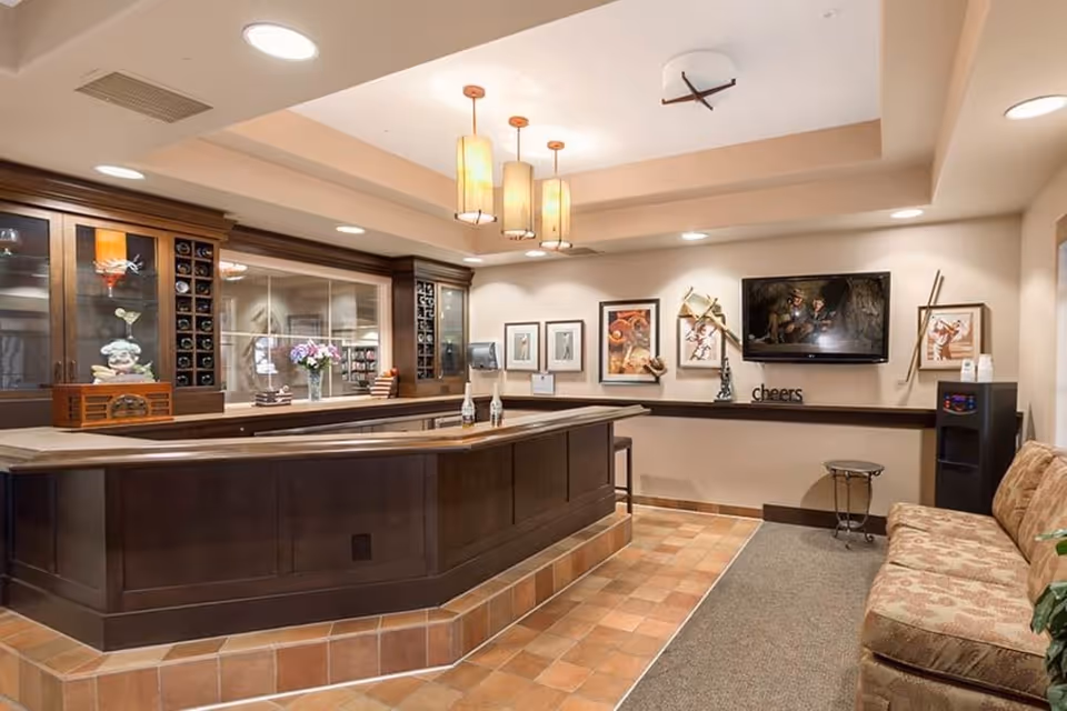 Interior communal lounge with a wooden reception-style bar, pendant lights, wall art, a TV, and seating.