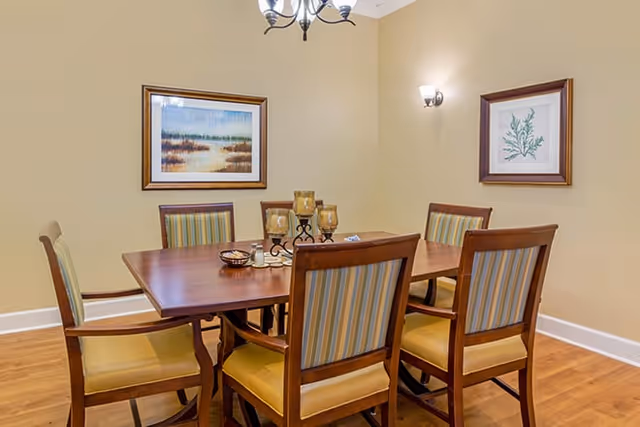 Dining room with a wooden table surrounded by six upholstered chairs, a candle centerpiece, and framed artwork on the walls.