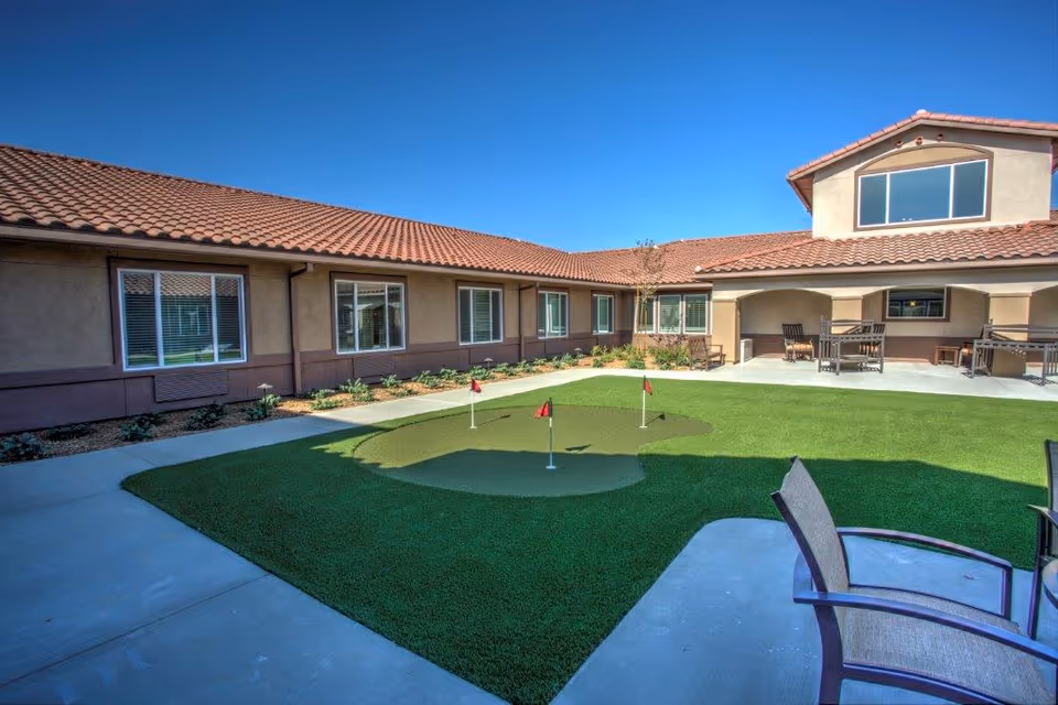 Courtyard at Vineyard Place featuring an artificial putting green, patio seating, and a tile-roofed building under a clear blue sky.