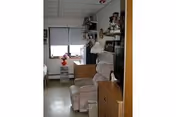 Small furnished living room with a recliner, TV, dresser, shelving and a window with blinds.