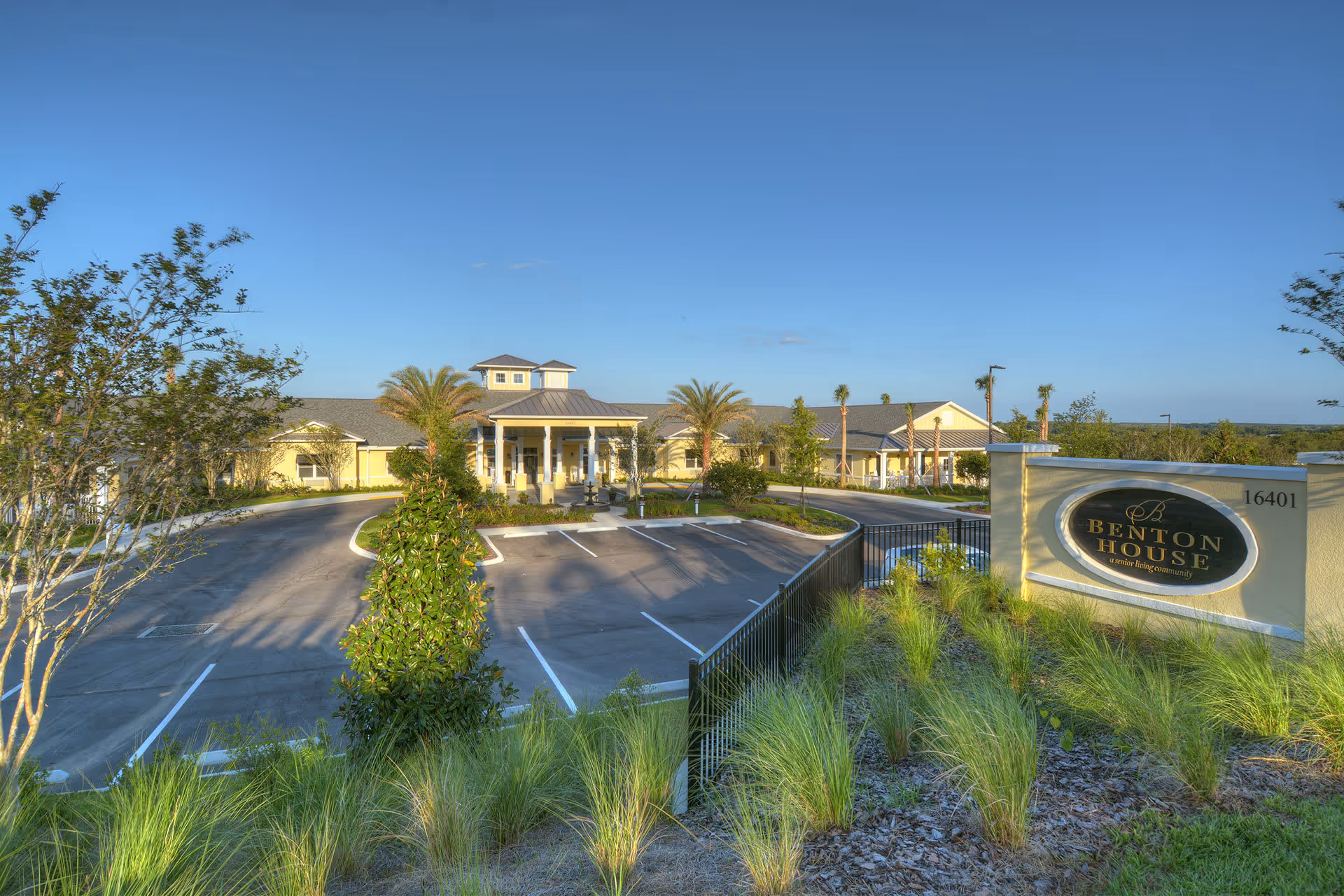 Front entrance and driveway of the Benton House senior living facility with landscaped grounds, palm trees, and a large facility sign.