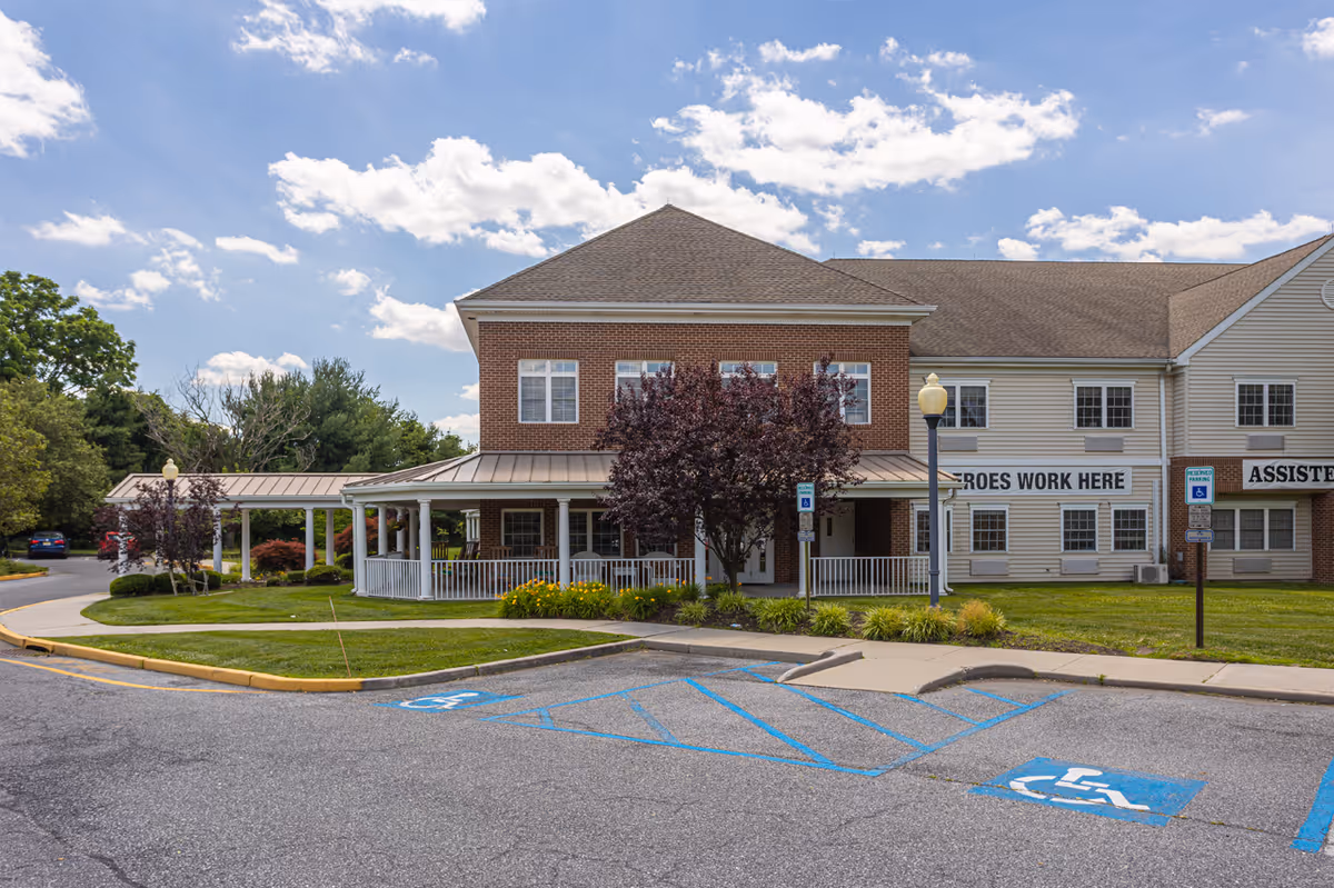 Front exterior of a senior living facility with a covered porch, landscaping, and marked handicap parking spaces.