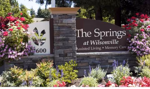 Stone sign reads The Springs at Wilsonville with flowers and landscaping.
