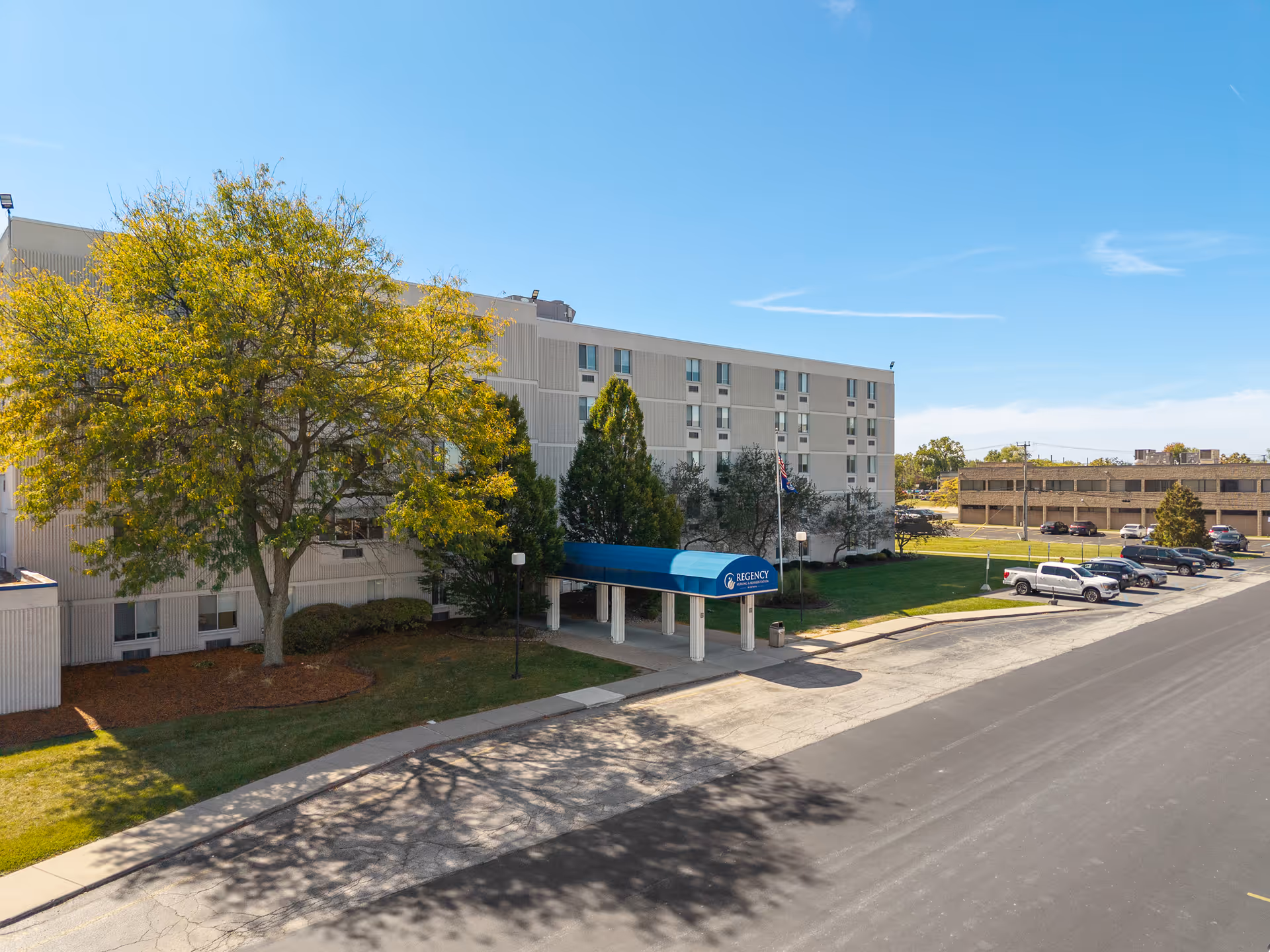 Exterior view of the Regency, a Villa Center senior living facility with a canopy entrance and surrounding greenery.