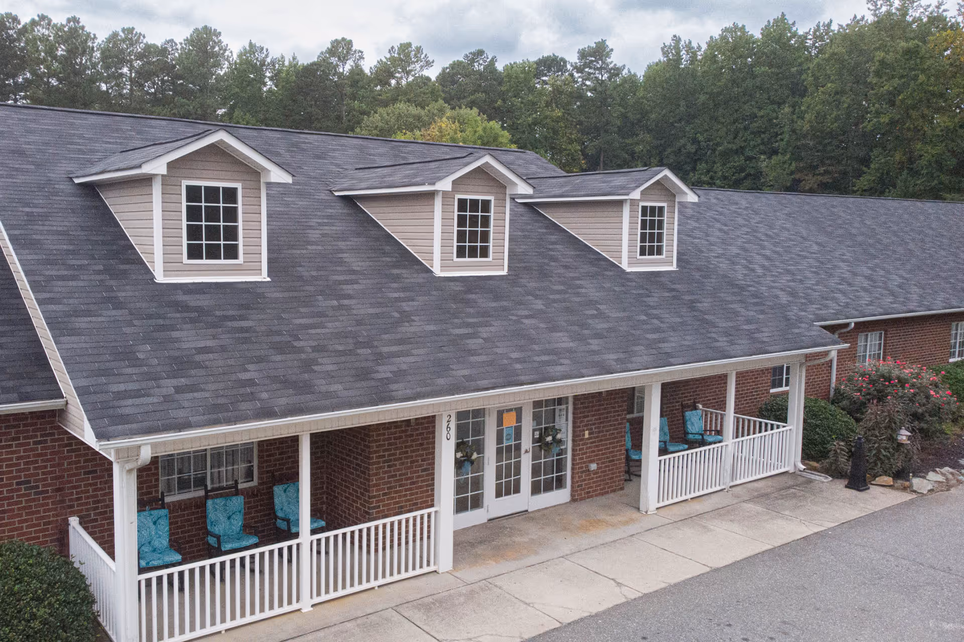 Exterior view of a brick senior living facility with a covered front porch and teal chairs.