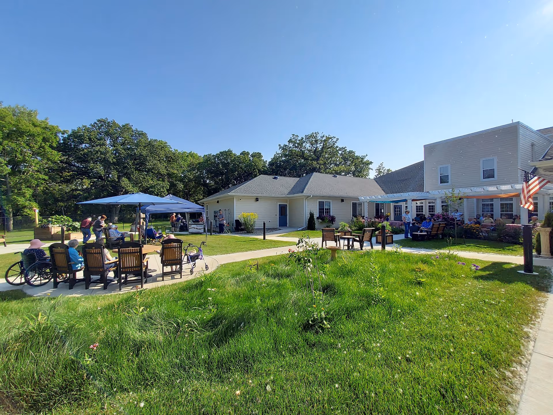 Outdoor courtyard at Birchwood Cottages with seniors seated in chairs under umbrellas and a low two-story building in the background.