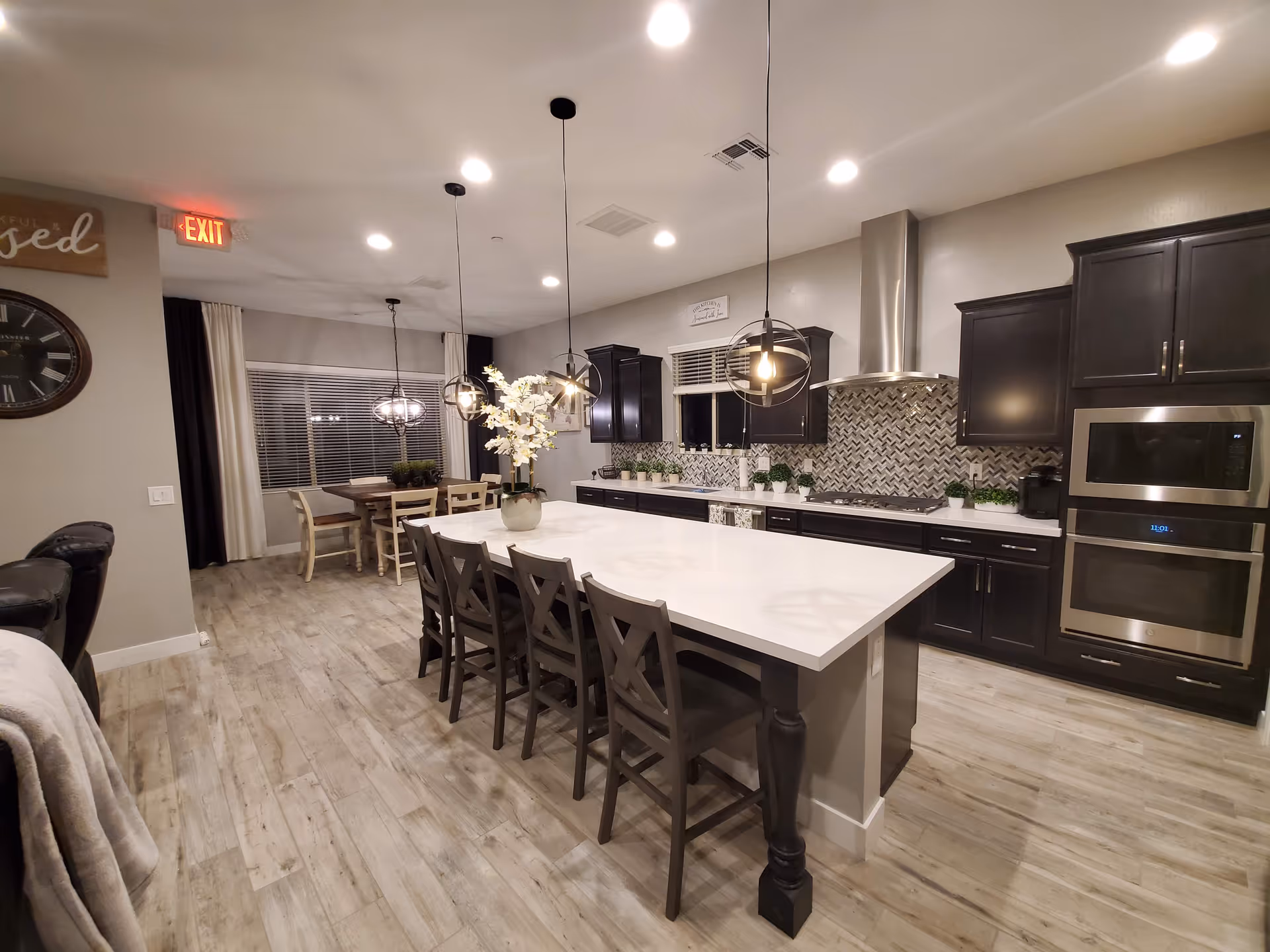 Modern open-plan kitchen with a large white island, dark cabinets, pendant lights, and an adjacent dining area.