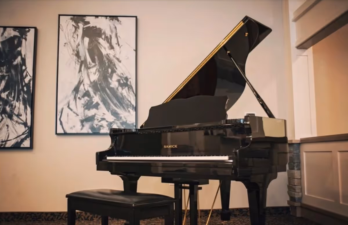 A black grand piano with a bench in a decorated interior space with abstract wall art on the wall.