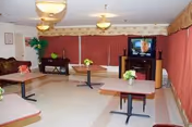 Indoor common lounge area at Shields Nursing Center Inc with tables, chairs, and a TV.