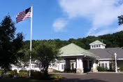 Front exterior of Arbor Ridge at Brookmeade with entrance, flagpole, and trees.
