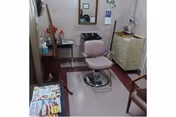 Small salon-style interior with a pink barber chair facing a wall mirror, storage cabinets, a cart, and a table with magazines.