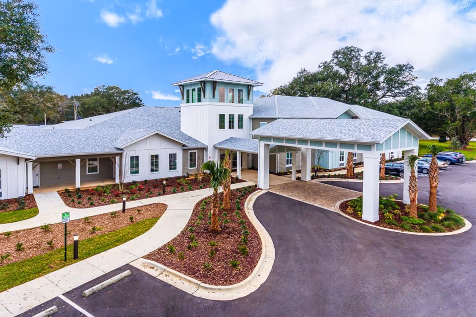 Front entrance of a single-story senior living facility with a covered porte-cochère, landscaped driveway, and parking area.