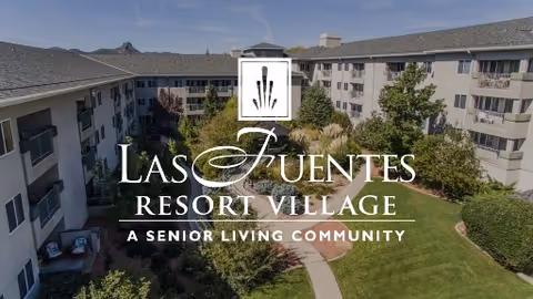 Courtyard with a central fountain, lawn and trees surrounded by a multi-story senior living building.