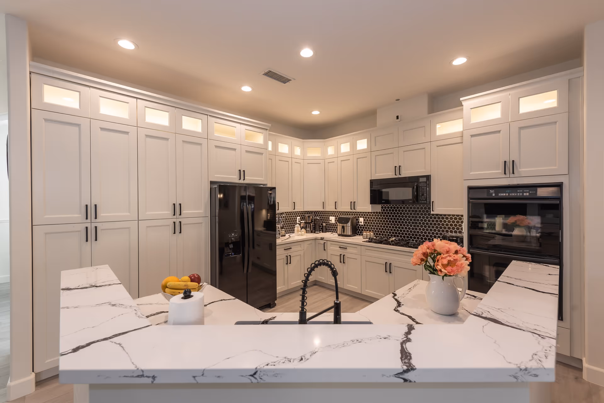 Bright modern kitchen with white cabinetry, marble-patterned island countertop, black appliances, and a vase of flowers.
