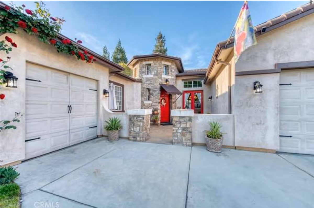 Front exterior of a stucco home with two garages and a stone entryway featuring a red front door.