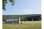 Front lawn with a stone sign reading "Mountain View" and the senior living building set against a tree-covered hill under a blue sky.