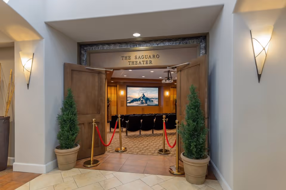 Open double doors into The Saguaro Theater showing rows of seats and a screen, flanked by potted plants and red ropes.