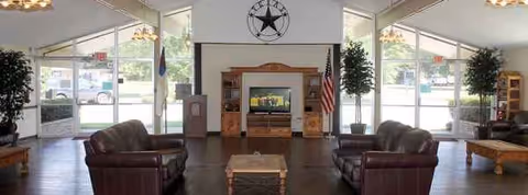 A spacious senior living lobby with leather couches, a fireplace, plants, and an American flag.