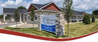 Exterior view of the Hampton Manor senior living facility entrance featuring a stone sign, manicured lawn, and single-story buildings.