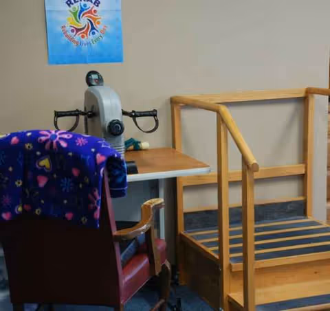 Interior care room with a chair, wooden lift frame, and an assistive device on a desk.