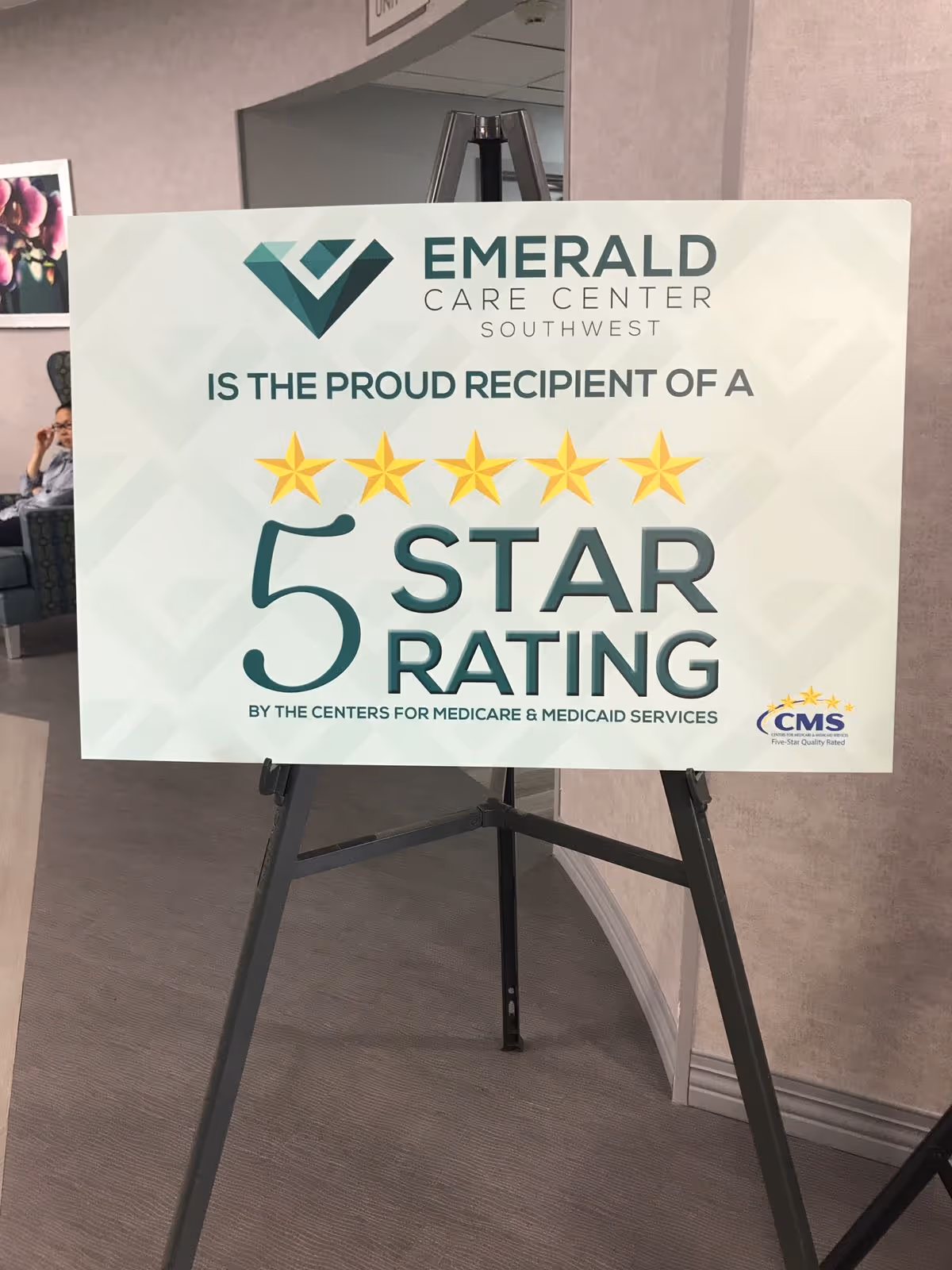 A sign on an easel inside a facility that reads 'Emerald Care Center Southwest is the proud recipient of a 5 star rating by the Centers for Medicare & Medicaid Services' with five gold stars and the CMS logo in the bottom right corner.