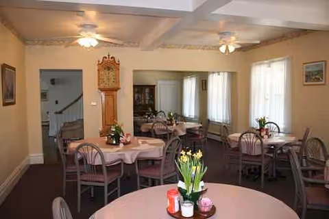 An interior dining room with round pink tablecloth tables, chairs, and a tall grandfather clock.