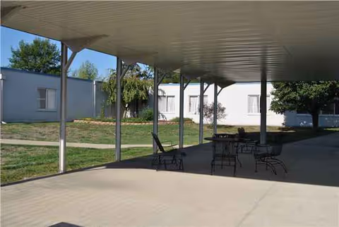 Covered outdoor patio with metal chairs and tables beside a white building.