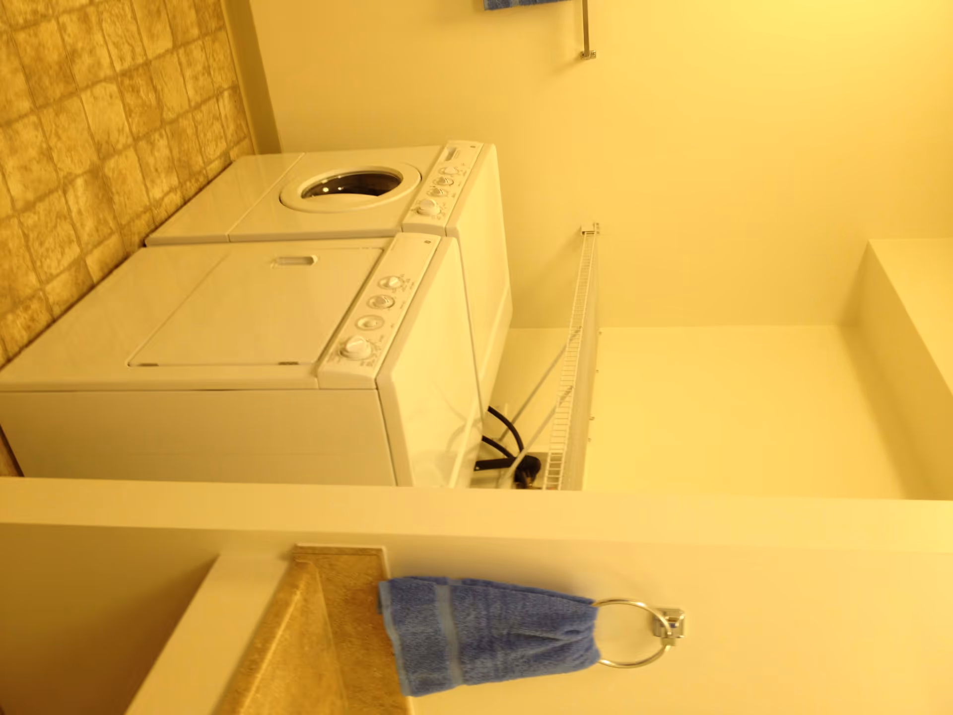 Laundry room with a white washing machine and dryer side by side, a beige countertop with a blue hand towel hanging on a ring, and a tiled floor.