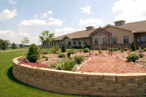 Exterior view of Anam Care, Inc. facility with a curved stone wall and landscaped courtyard.