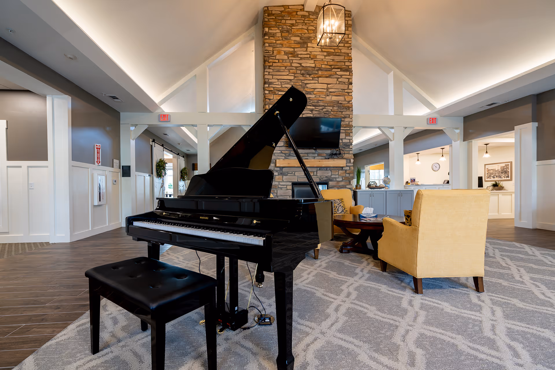 Spacious lounge with a black grand piano, yellow armchairs, stone fireplace with TV, and a vaulted ceiling.
