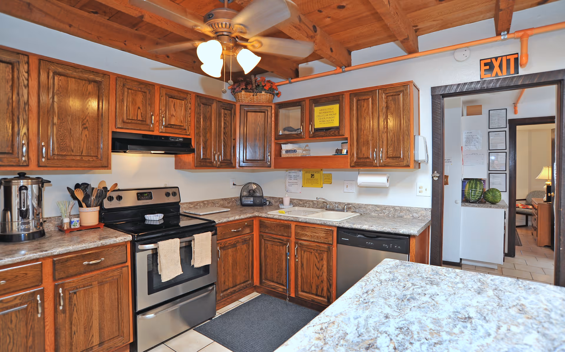 A well-lit kitchen with wooden cabinets, stainless steel appliances, a ceiling fan, and granite countertops.
