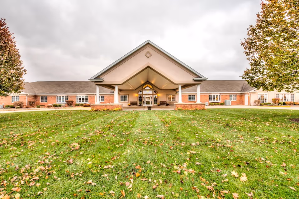 Front entrance of a single-story brick senior living facility with a covered porte-cochère and a grassy lawn in the foreground.