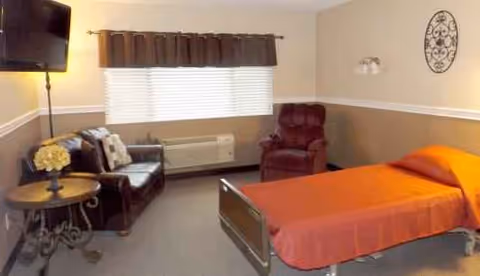 A cozy senior living bedroom with orange bedspread, seating area, and window.