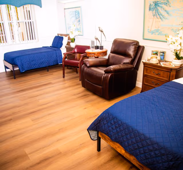 Shared bedroom with two twin beds, a leather recliner, side tables, and wood-look flooring in a senior residence.
