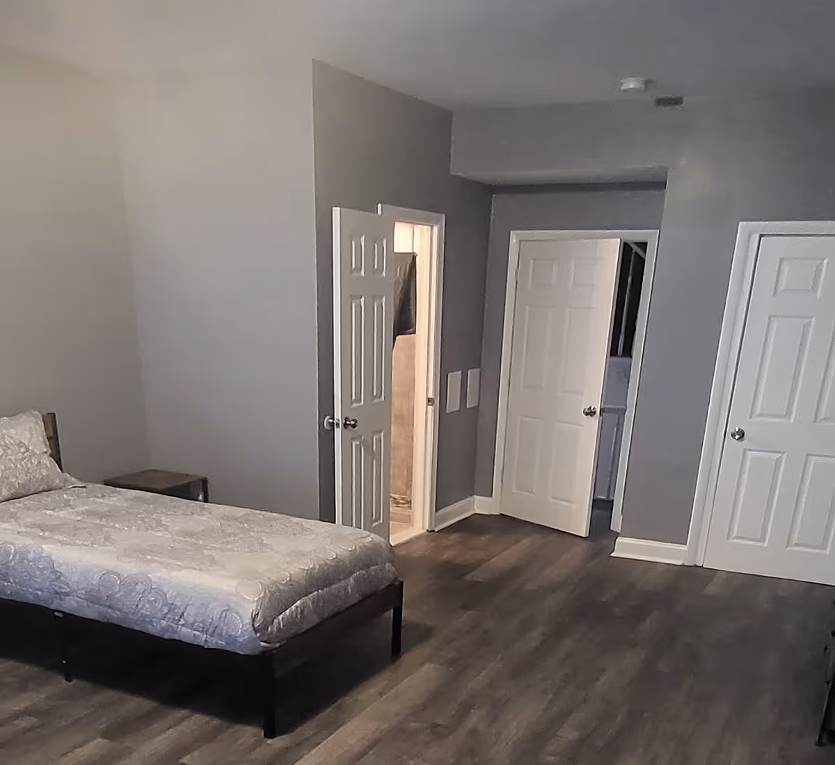 A sparsely furnished bedroom in a senior living facility with a bed and several doors.