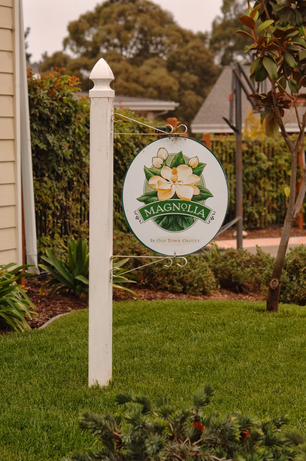 A sign for Magnolia in Old Town Orcutt with a floral design and green background.