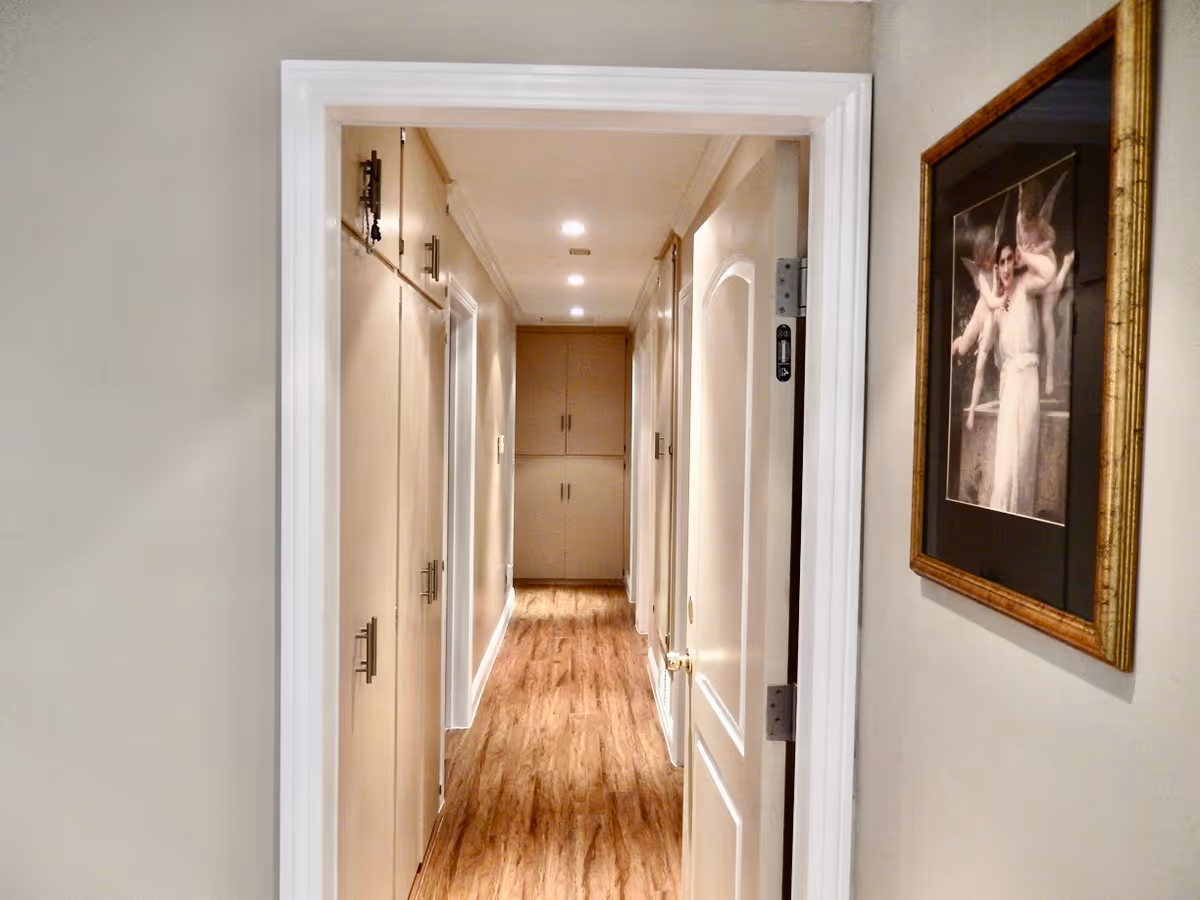 View down a well-lit interior hallway with hardwood floors, built-in cabinets on the left and a framed painting on the right wall.