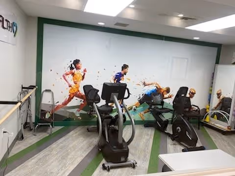Exercise room with several cardio machines in front of a mural of runners on the wall.