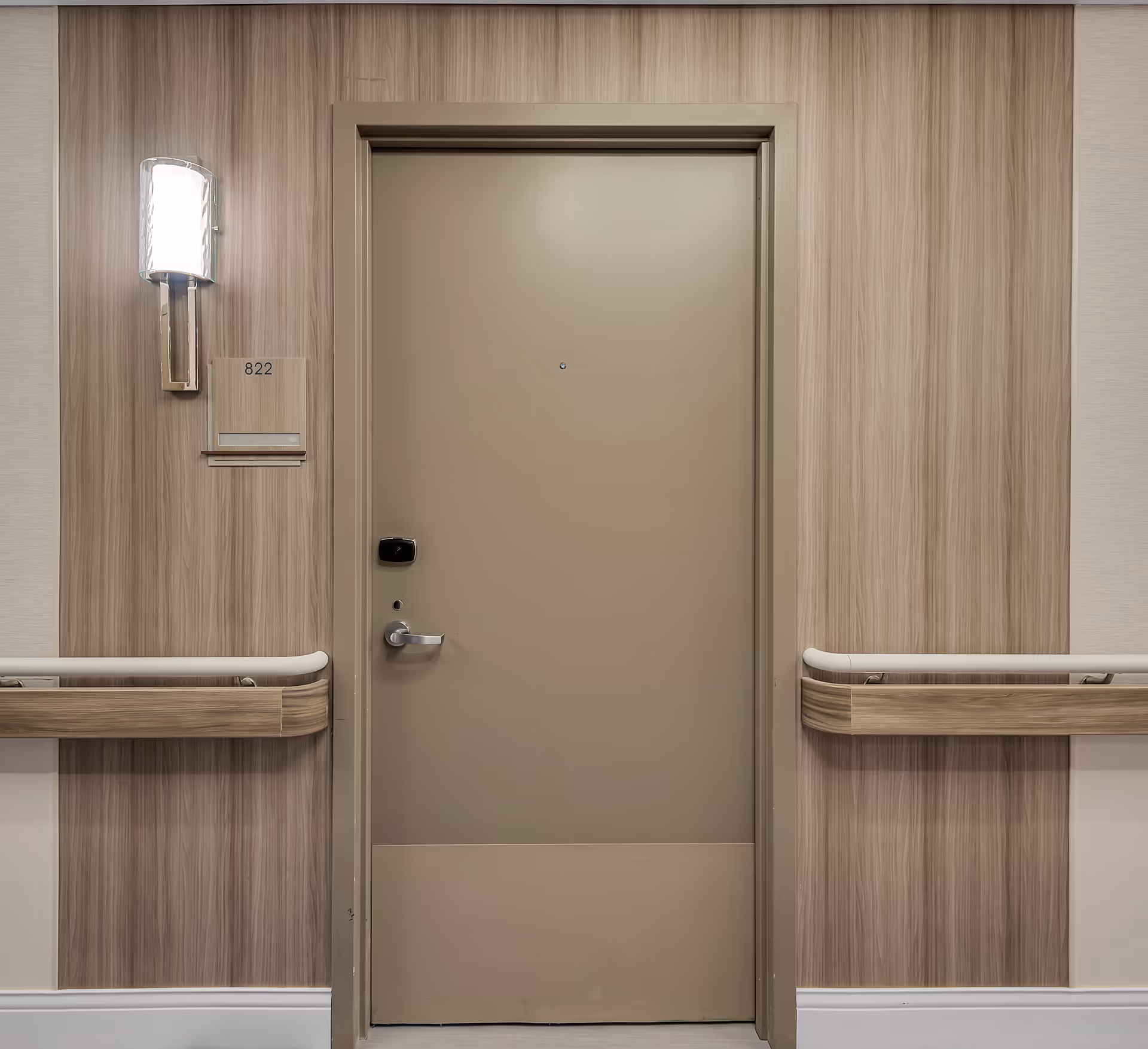 Closed beige apartment door numbered 822 in a hallway with wood-paneled walls, handrails, and a wall sconce.